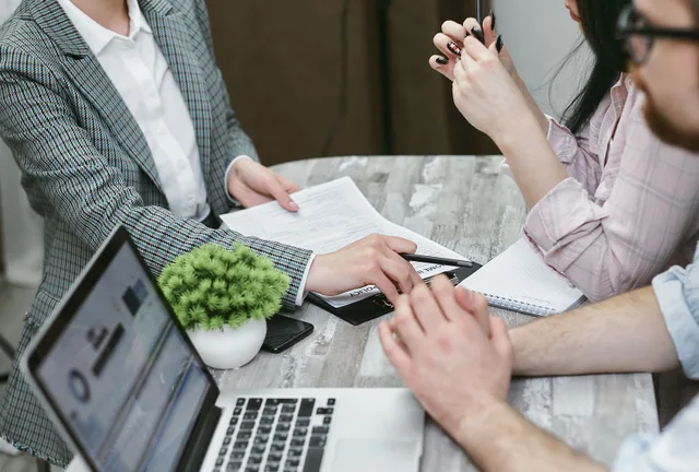 Professional meeting discussing business agreements with laptops and documents on a rustic table. Corporate event planning startup: legal setup to event chain