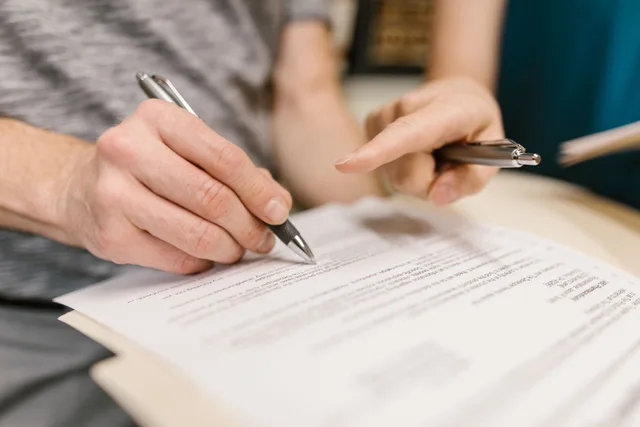 Close-up of two adults reviewing and signing a legal document with pens indoors. How to Negotiate Hotel Attrition Clauses in a Conference Contract