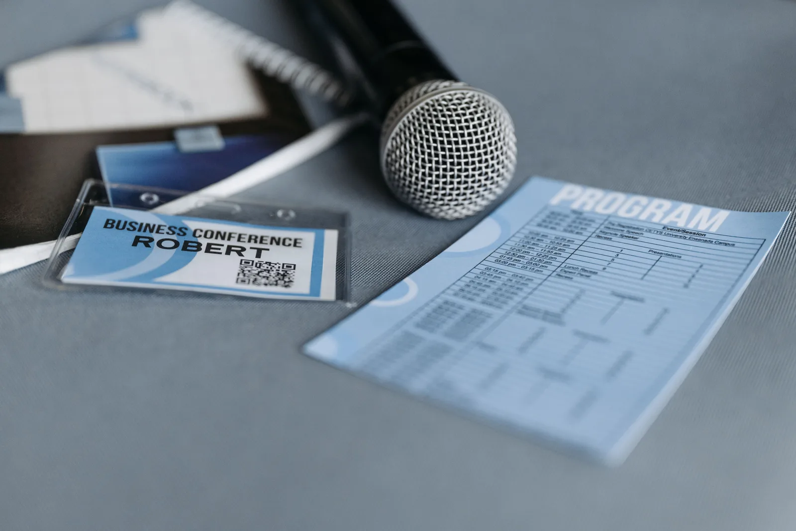 Close-up of a microphone, name tag, and program guide on a table at a business conference. Should a corporate event planning business buy new or used equipment