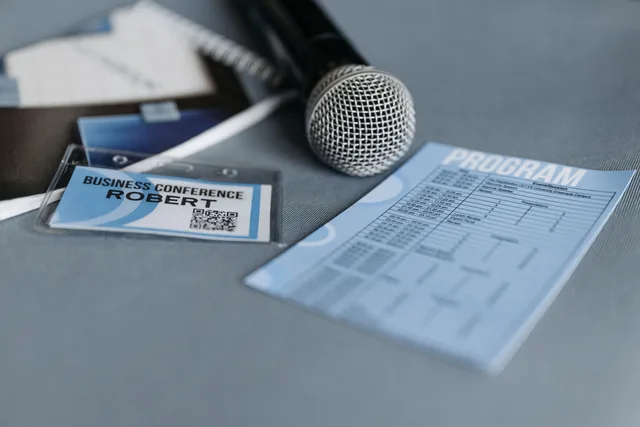 Close-up of a microphone, name tag, and program guide on a table at a business conference. Should a corporate event planning business buy new or used equipment